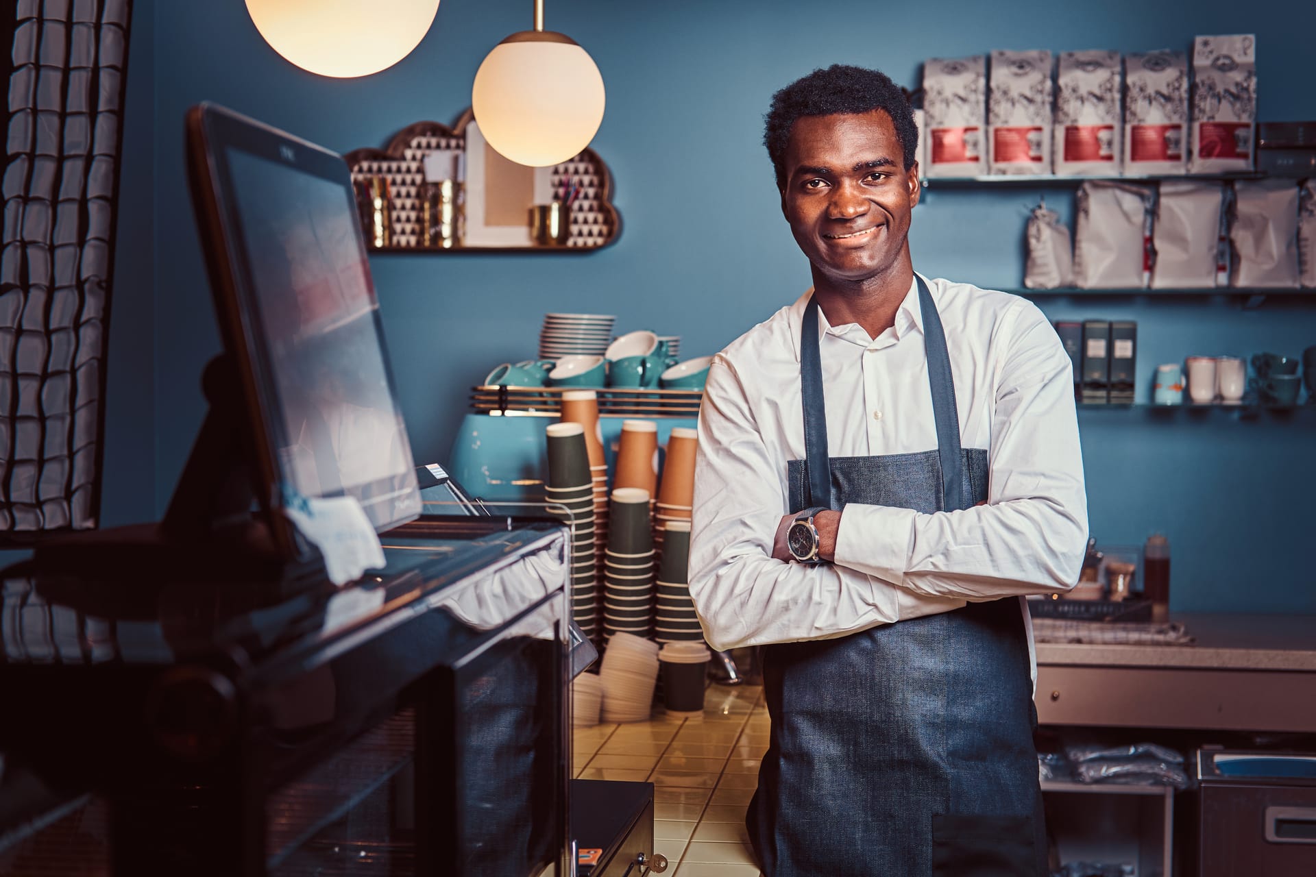 A barista standing with arms crossed behind the counter of a coffee shop